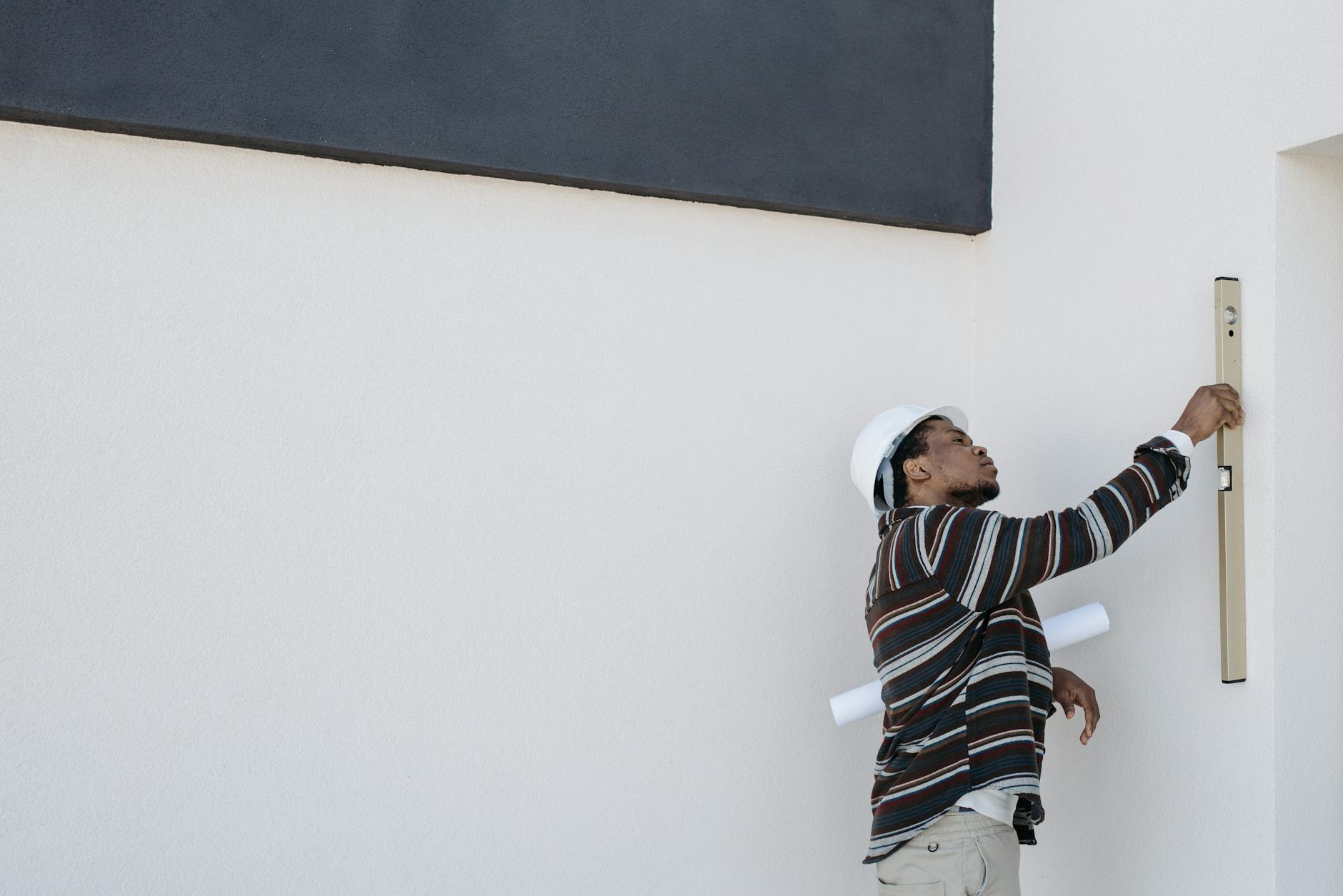 Architekt w kasku sprawdza pion ściany poziomicą przed ociepleniem