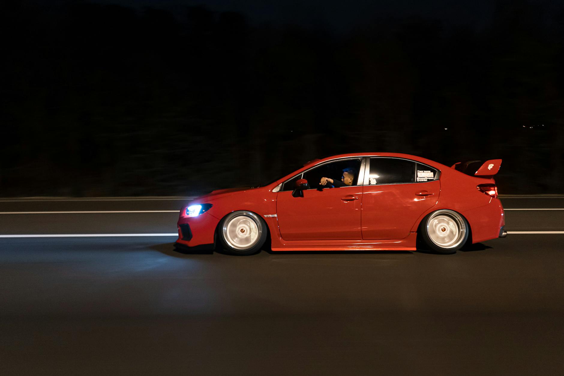 Czerwony sportowy samochód pędzi nocą autostradą z rozmytym tłem