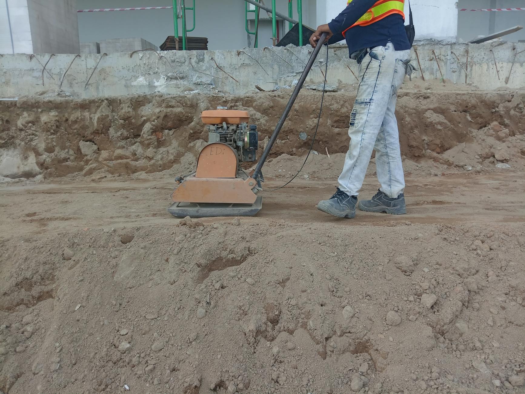 Pracownik budowlany zagęszczający grunt zagęszczarką na działce