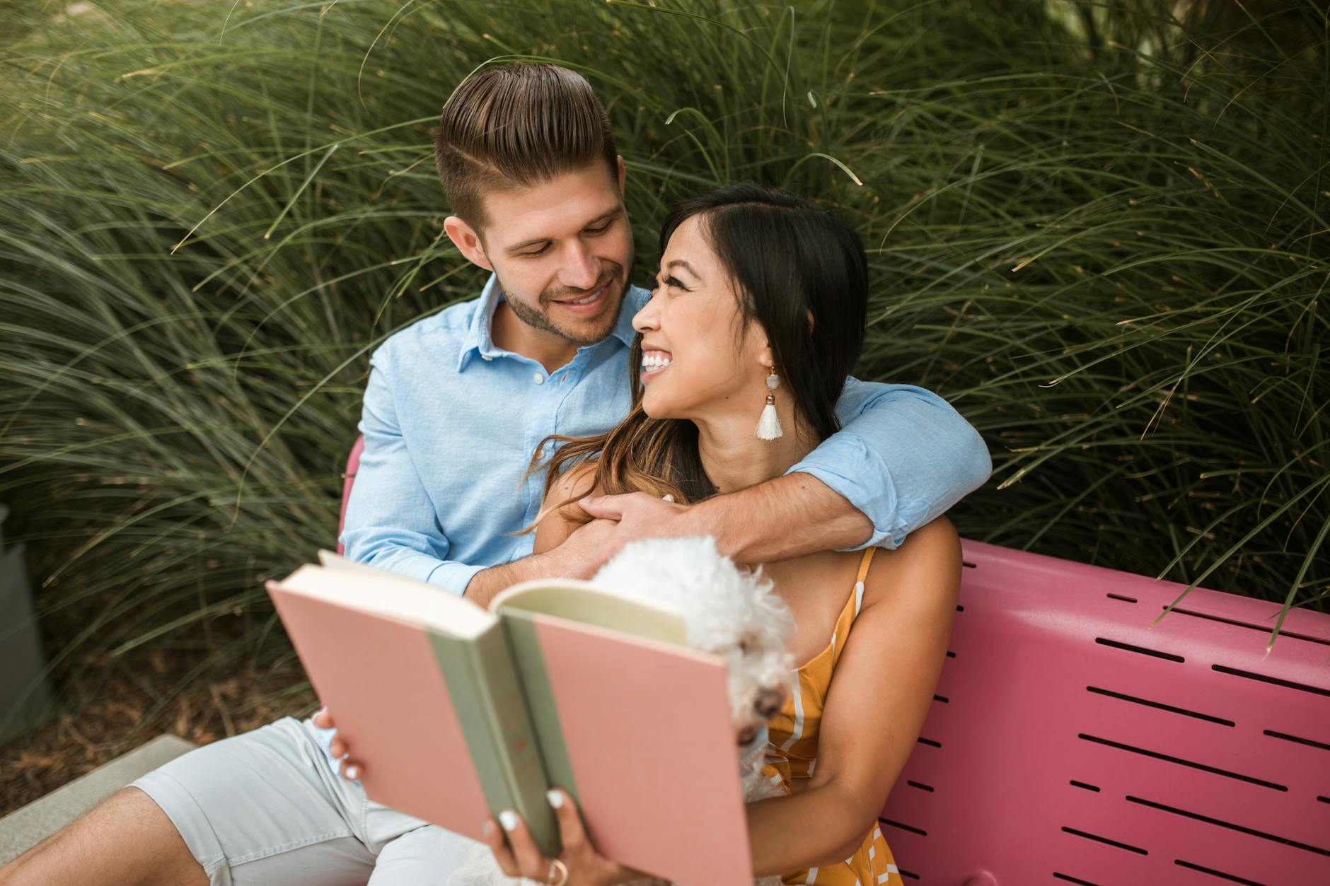 Uśmiechnięta para różnych ras czyta wspólnie książkę w parku