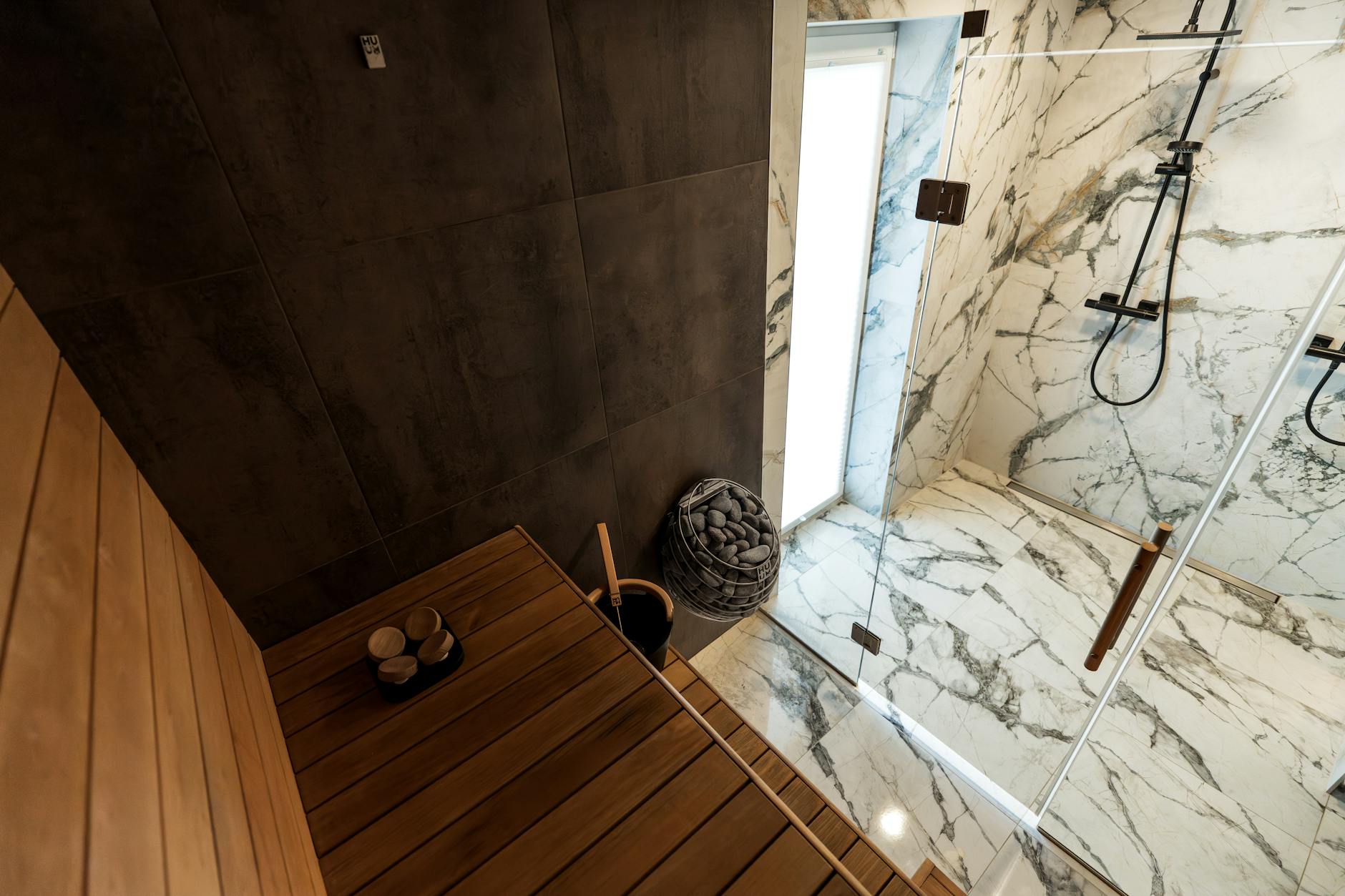 Nowoczesna sauna z przeszklonym wejściem obok marmurowego prysznica