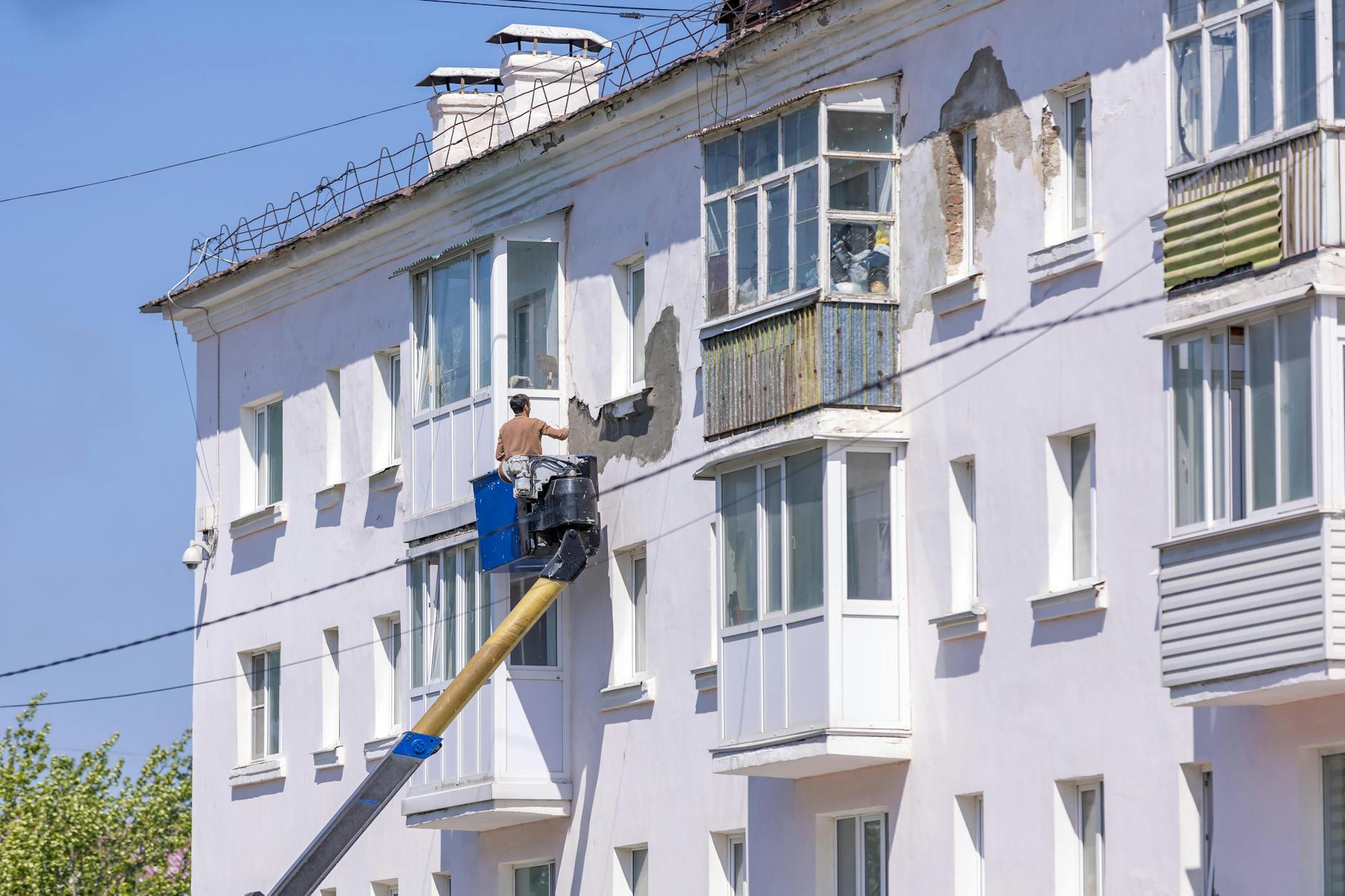 Tynk silikonowy czy silikatowy na elewację? Różnice, których nie widać w próbniku Pracownik na podnośniku odnawia elewację budynku w słoneczny dzień