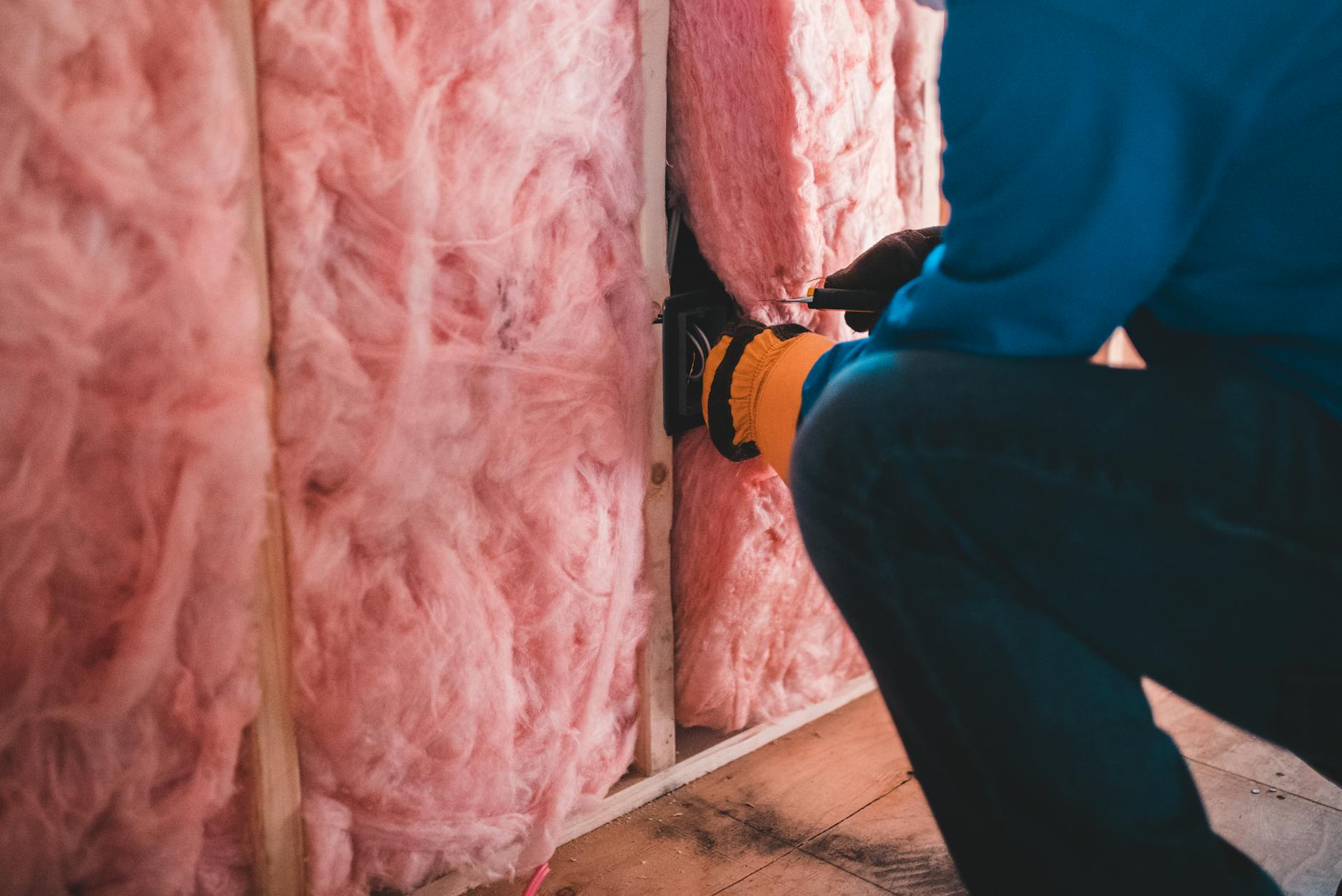 Pracownik w rękawicach montuje różową izolację z wełny mineralnej