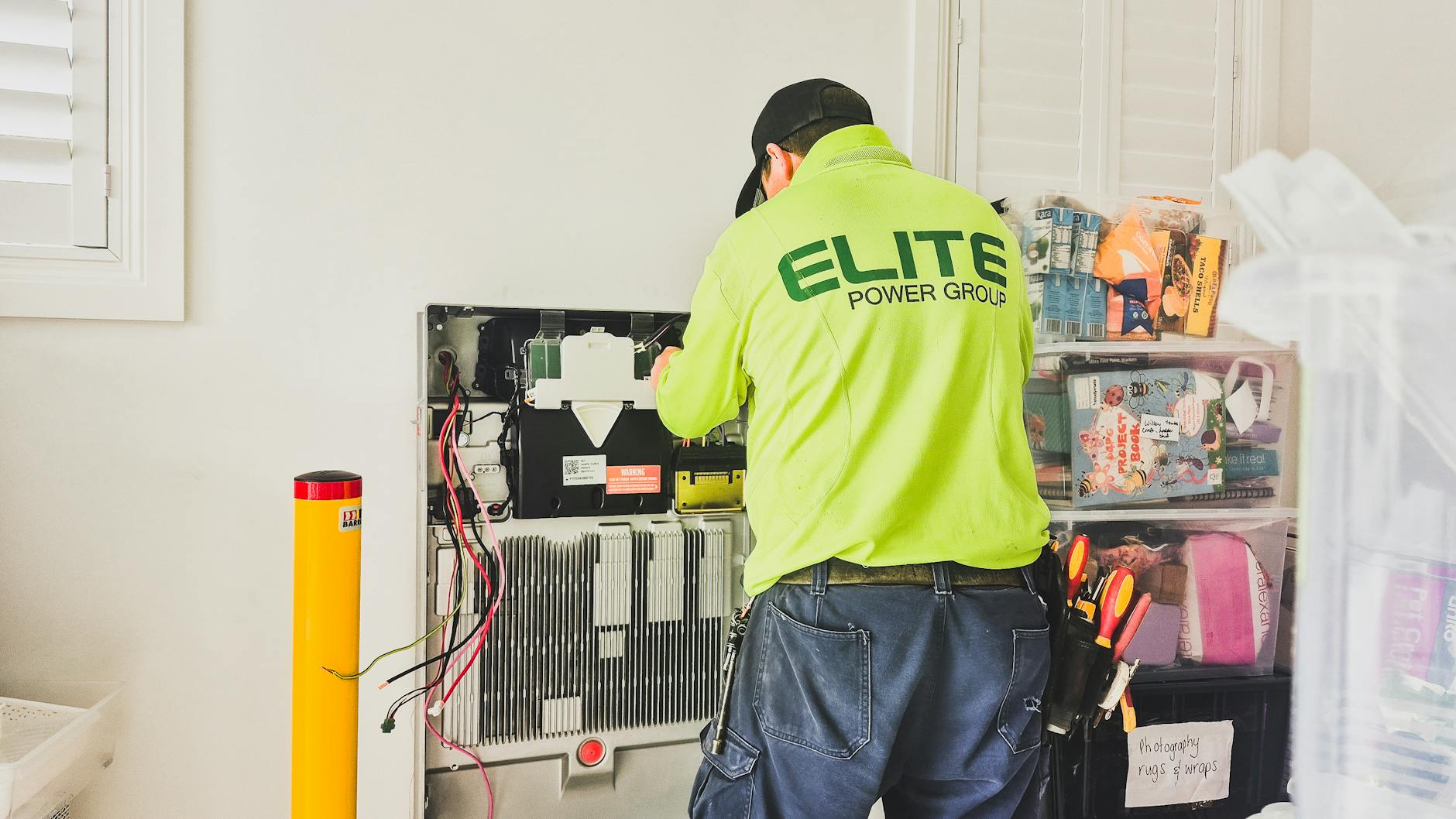 Magazyny energii w OZE: jak dobrać pojemność i moc, aby zwiększyć autokonsumpcję i opłacalność inwestycji Technik montujący domowy magazyn energii przy ścianie wewnątrz budynku