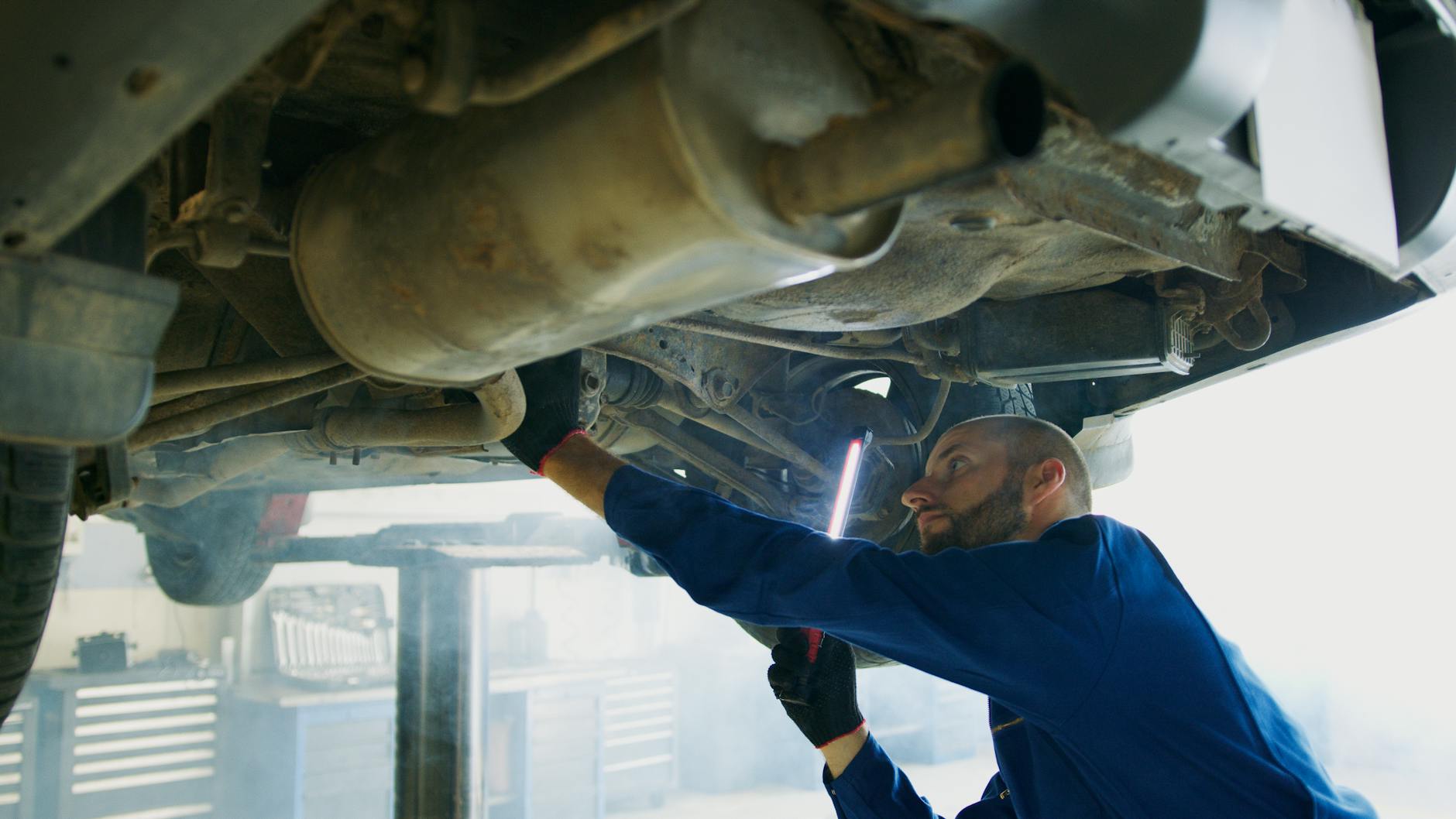 Jak rozpoznać zużyty katalizator i kiedy opłaca się go wymienić lub sprzedać Mechanik pod samochodem sprawdza układ wydechowy w warsztacie