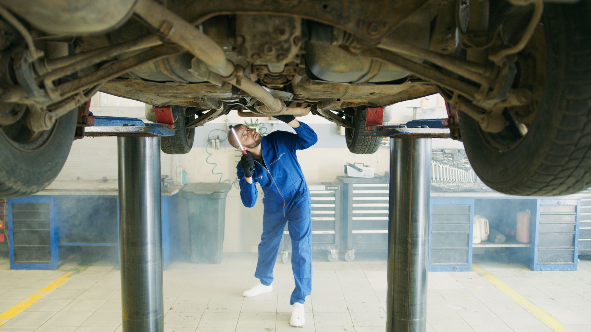 Mechanik w niebieskim kombinezonie ogląda samochód na podnośniku w warsztacie