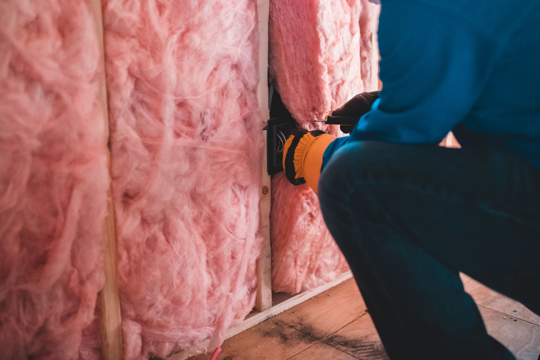 Pracownik montuje różową wełnę mineralną na ścianie domu