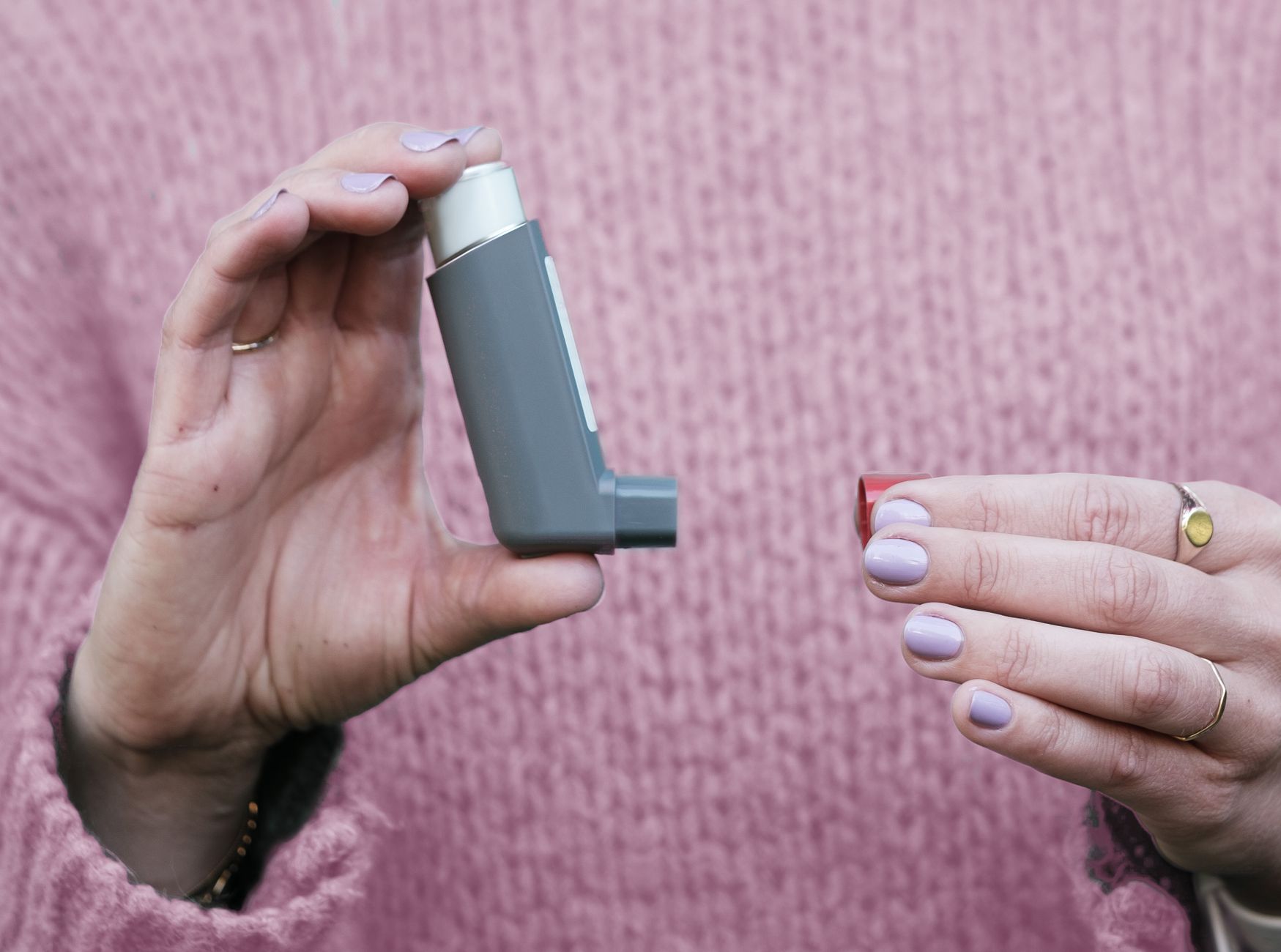 Kobieta trzyma szary inhalator przy różowym swetrze